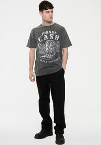 Gray cotton T-shirt featuring a graphic of cowboy boots and "Johnny Cash" text. Paired with black trousers and black boots.