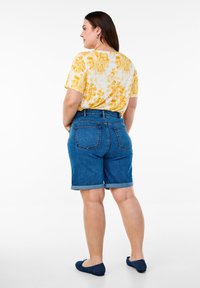 Camisa de manga corta con estampado floral amarillo combinada con pantalones cortos de mezclilla de tiro alto. Los pantalones cortos presentan un dobladillo enrollado y bolsillos traseros.