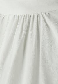 Tessuto bianco con texture e pieghe, che mostra motivi sottili. La parte superiore liscia si collega alla parte inferiore fluente, creando una silhouette morbida.