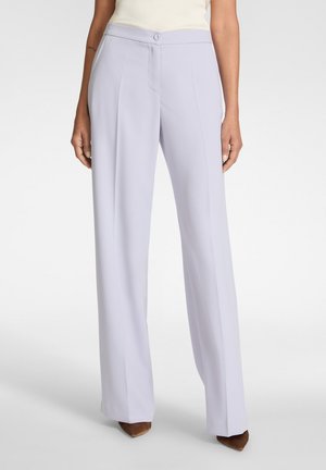 Vrouw draagt lavendelkleurige, hoog getailleerde broek met wijde pijpen en voorplooien, en een met knopen gesloten tailleband, gecombineerd met bruine puntige schoenen.