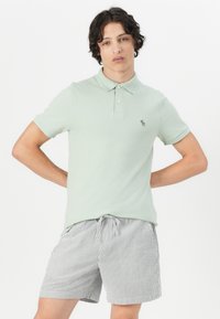 Light green polo shirt with short sleeves, two buttons, and small logo. Paired with striped shorts featuring a drawstring waist.