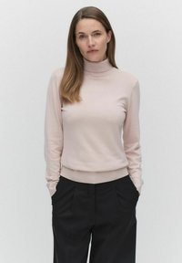 Lichtroze coltrui gemaakt van zachte stof, met lange mouwen en een getailleerde taille, gecombineerd met zwarte high-waisted broek.
