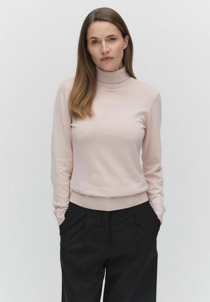 Lichtroze coltrui gemaakt van zachte stof, met lange mouwen en een getailleerde taille, gecombineerd met zwarte high-waisted broek.