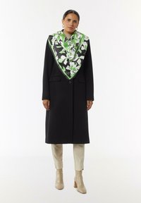 Czarny płaszcz z dwoma przednimi kieszeniami i jednym guzikiem, w zestawieniu z dużym jedwabnym szalem w zielono-czarny kwiatowy wzór. Beżowe botki za kostkę.