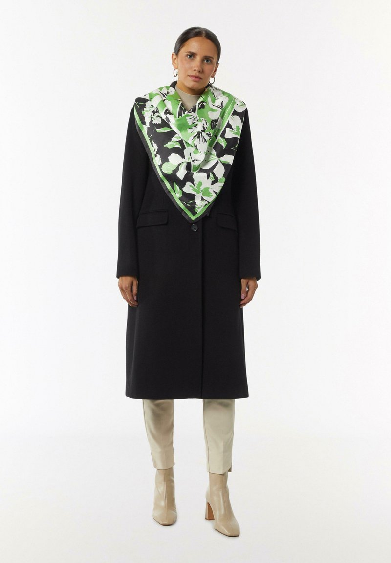 Czarny płaszcz z dwoma przednimi kieszeniami i jednym guzikiem, w zestawieniu z dużym jedwabnym szalem w zielono-czarny kwiatowy wzór. Beżowe botki za kostkę.