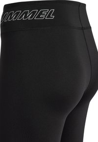 Nahaufnahme von schwarzen enganliegenden Leggings mit sichtbaren Nähten und weißem "HUMMEL"-Logo am Bund.
