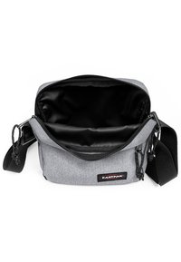 Grå tyg axelväska med dragkedjestängning, svart innertyg, justerbar rem och Eastpak-logotyp fram.