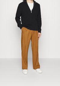 Maglione nero a costine con colletto a mezza zip abbinato a pantaloni larghi color sabbia, completato da sneakers bianche per un look casual.