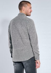 Grauer Pullover mit strukturierter Oberfläche, hohem Kragen, langen Ärmeln und Knopfakzenten, mit leicht lässiger Passform und gerippten Details an den Bündchen.