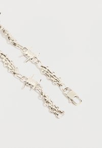 Δύο άκρα ασημένιου αλυσιδωτού κολιέ με κούμπωμα αστακού και κλείσιμο τύπου τογκλ σε ανοιχτό φόντο, που δείχνουν λεπτομερείς μεταλλικούς κρίκους και συνδέσμους.