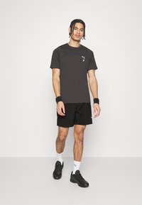 Camiseta atlética negra con logotipo, de manga corta y diseño raglán. Combinada con pantalones cortos negros y zapatillas deportivas negras para un look coordinado.
