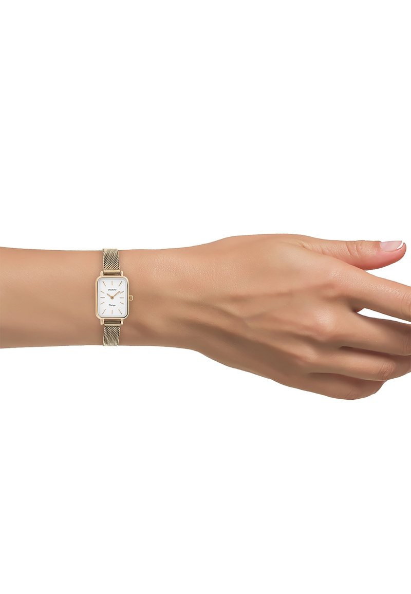 Montre rectangulaire avec un cadran blanc, bracelet en maille dorée et index horaires minimalistes. La montre est portée au poignet d'un teint de peau naturel.