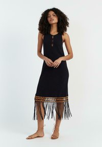 Zwarte jurk tot de knie met een ronde halslijn, een open sleutelgatdetail en een franjeszoom met bruin beads. Draag het met tan sandalen.