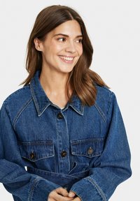 Tmavomodrá džínsová bunda s dvoma náprsnými vreckami a gombíkmi. Má golier a páskový pás. Textúrovaná tkanina, pohodlný strih.