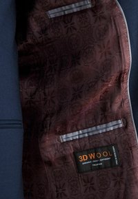 Wnętrze marynarki w kolorze granatowym z bordowym wzorzystym podszewką, szarym akcentem na kieszeni oraz metką z napisem "3D WOOL DYNAMIC DAILY DIFFERENT TOLLEGNO."