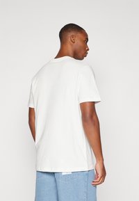 Hvit bomulls t-skjorte med rund hals og korte ermer, med en avslappet passform og minimalistisk design, vist fra en bakvinkel.
