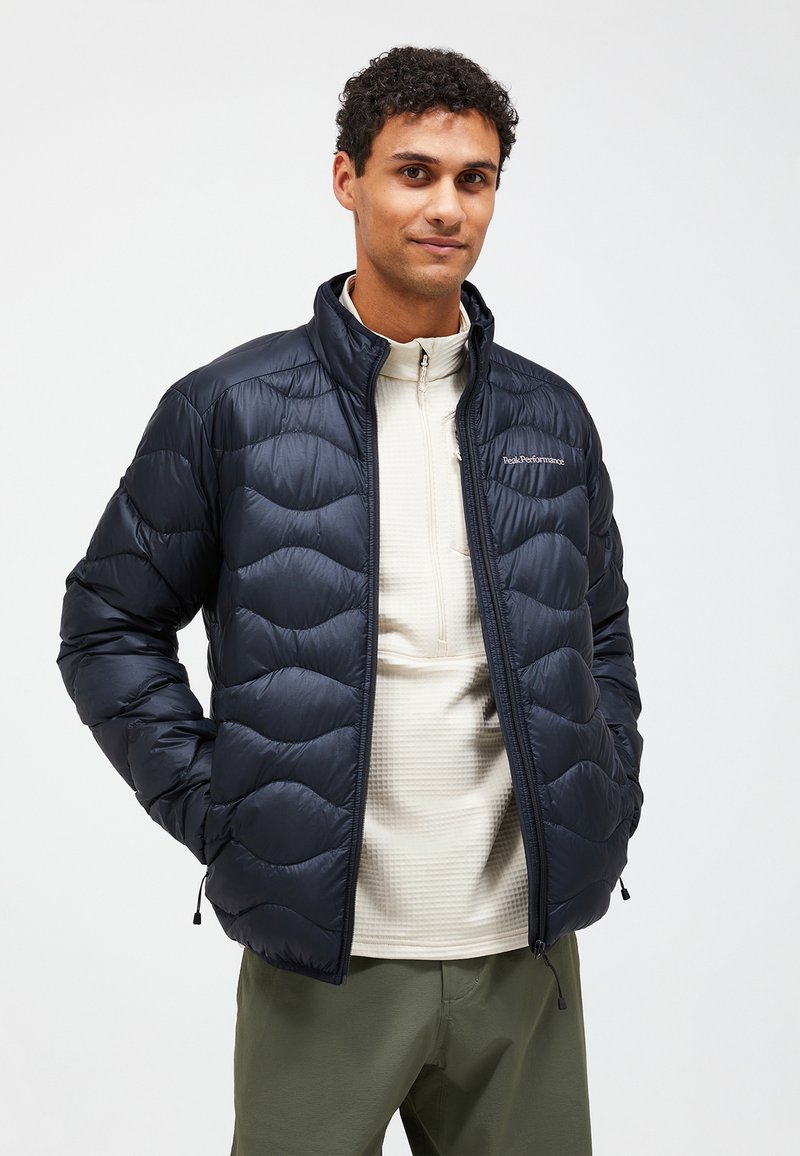 Veste matelassée marine avec un motif de vagues, fermée par zip et avec un col haut. Portée par-dessus une couche de base texturée et de couleur claire avec un design à demi-boutons.