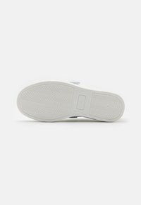 Suela de zapatilla blanca con patrón de espiga, material de goma texturizado, puntera redondeada y detalle de marca sutil cerca del talón.