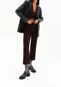 Zwarte leren blazer over een rode en zwarte geblokte crop top en bijpassende broek. Stevige zwarte loafers met grijze sokken maken de look compleet.