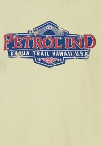 Světle žluté tričko s modrou a červenou grafikou, na které je vyraženo "PETROLIND" a "KAHUA TRAIL HAWAII U.S.A." v retro stylu.
