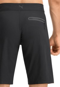 Schwarze Sportshorts aus glattem, dehnbarem Stoff. Enthält eine Reißverschlusstasche auf der Rückseite und ein dezentes Logo in der Nähe des Bundes.