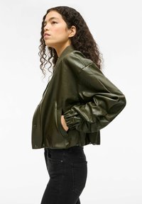 Olivgrüne Lederbomberjacke mit lockerem Schnitt, elastischen Bündchen, Seitentaschen und Reißverschluss, kombiniert mit schwarzen Jeans.