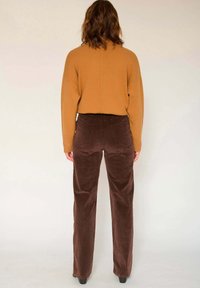 Pantalon en velours côtelé marron à jambe droite, associé à un pull côtelé moutarde. Le pull a un col rond et des épaules tombantes.