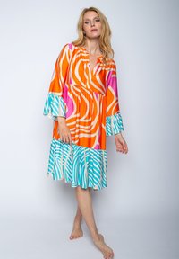 Kleurvolle jurk met oranje, roze en blauwe golvende patronen. Lange klokmouwen en een gelaagde onderkant voegen visuele textuur toe.