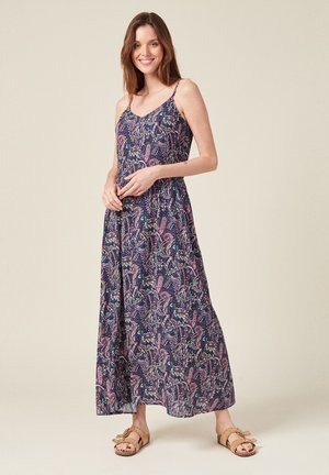 Abito lungo con base blu navy e motivo paisley colorato. Presenta spalline sottili e una vestibilità ampia, abbinato a sandali beige. Tessuto di trama liscia.