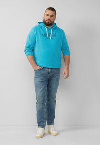 Turkusowa bluza z kapturem i sznurkiem z nadrukowanym logo; w połączeniu z jasnoniebieskimi dżinsami i białymi sneakersami z beżowymi podeszwami; swobodny styl.