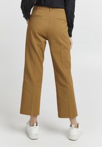 Pantalons larges en tissu beige, avec une taille haute, deux poches arrière et une texture lisse. Associés à des baskets blanches.
