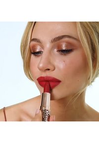 Red lipstick with a leopard print case. The model applies it, showcasing a smooth texture and matte finish on full lips.