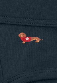 Ciemnoniebieska tkanina o gładkiej fakturze z małym haftowanym jamnikiem w czerwonej koszulce z białym wzorem.