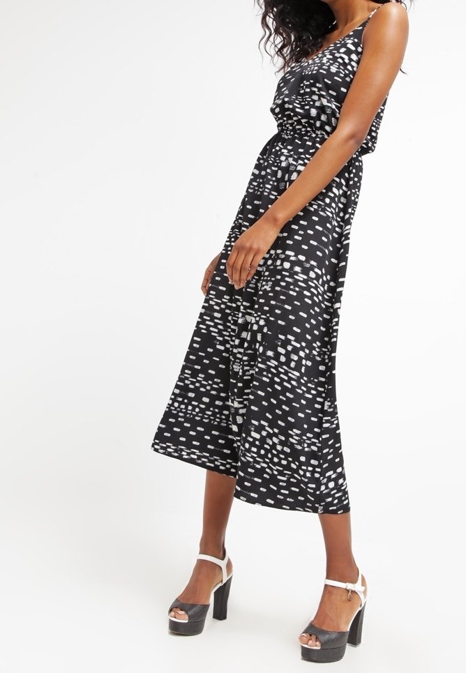 Black midi dress with white abstract patterns, sleeveless design, and cinched waist. Paired with chunky black platform heels and white ankle straps.