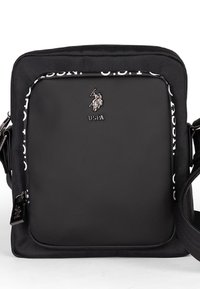 Svart axelväska med en slät yta, utrustad med en logotyp och vit text längs sidan. Justerbar rem ingår.