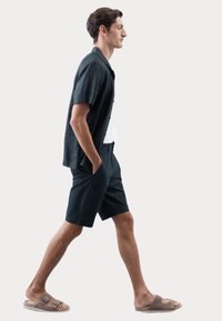 Camisa de manga corta de color navy y pantalones cortos a juego en tejido ligero, combinados con sandalias beige que cuentan con dos correas ajustables.