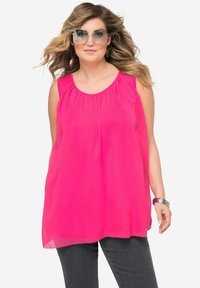 Blusa senza maniche fucsia con scollatura arricciata, realizzata in tessuto leggero. Indossata con jeans scuri e gioielli con dettagli argentati.