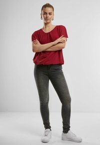 Rode blouse met korte mouwen en een ronde halslijn, voorzien van plooidetails, gecombineerd met strakke zwarte jeans en witte sneakers.