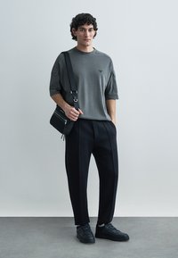 Grå oversize t-shirt med korta ärmar, kombinerad med svarta plisserade byxor och svarta sneakers. Har en liten logotyp på tröjan.