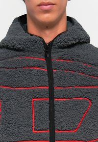 Gray fleece jacket with hood, featuring red stitch patterns and a front zipper. The texture is soft and fuzzy.