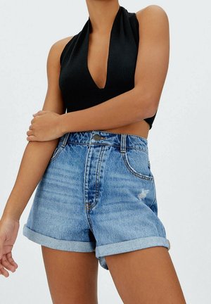 Light blue denim shorts with rolled cuffs, featuring a high waist, front button, and slight distressing. Black ribbed halter top.