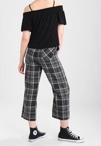 Černý top bez ramínek, zkrácený design. Šedé široké kalhoty s kostkovaným vzorem. Černé vysoké tenisky s bílou podrážkou a logem.