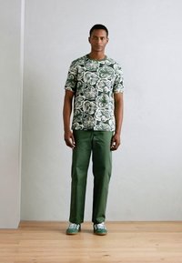 Short-sleeve green floral patterned shirt paired with green trousers and green-striped sneakers. Simple design, cotton material, relaxed fit.