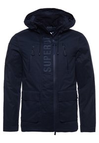Granatowa kurtka z kapturem, z przednim zamkiem błyskawicznym, dwoma kieszeniami na suwak na klatce piersiowej, dwiema kieszeniami z klapką, kieszenią na rękawie oraz logo "SUPERDRY" na klapie zamka.