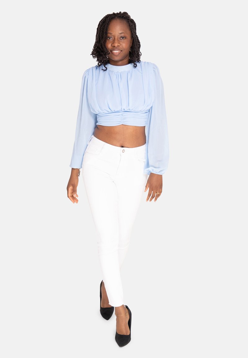 Blusa cropped azzurro chiaro con maniche a sbuffo, abbinata a jeans skinny bianchi e tacchi alti neri. Tessuto morbido, design aderente.