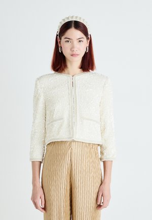 Cropped white textured jacket with bead embellishments and two front pockets, paired with gold pleated high-waisted trousers.