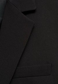 Tissu de blazer noir avec une texture lisse, présentant un col cranté et une poche poitrine unique dans un design ajusté classique.