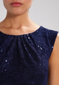Námořnický krajkový top s designem na ramínka, texturovaná látka s květinovým vzorem a rozptýlené flitry pro přidaný detail a lesk.