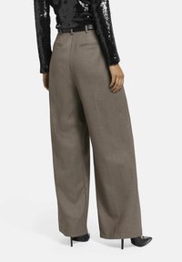 Royale-brede broek in een zachte taupe stof, met een getailleerde pasvorm, riemlussen en achterzakken, gecombineerd met een zwarte top met pailletten.