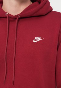 Bordo kapucar s vrvico, narejen iz mehke tkanine. Na prsih je bel Nike logotip. Gladek otip z rebrastimi manšetami.